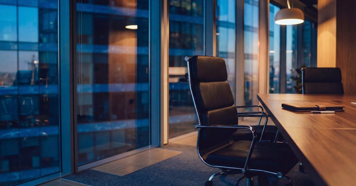 Black executive office chair beside a wood conference table in a modern office with floor-to-ceiling windows.