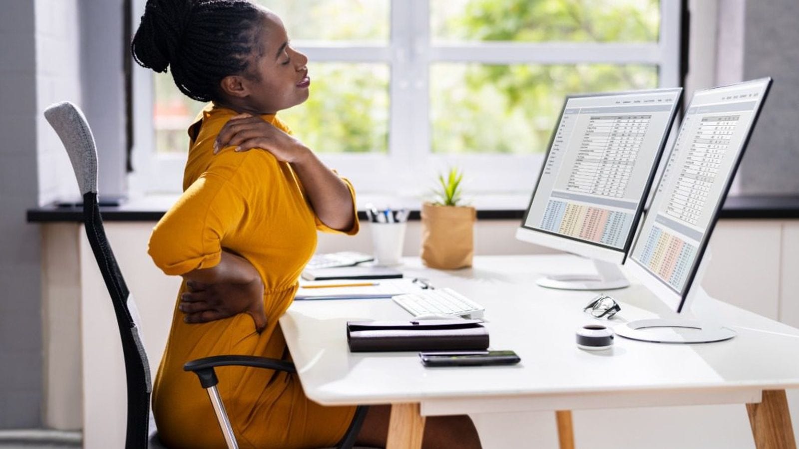 Office worker holding her back and shoulder in pain while seated at her desk