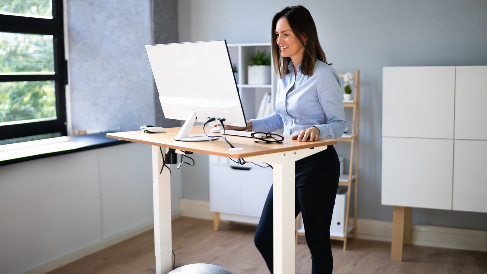 A woman happily works while standing at her office standing desk.