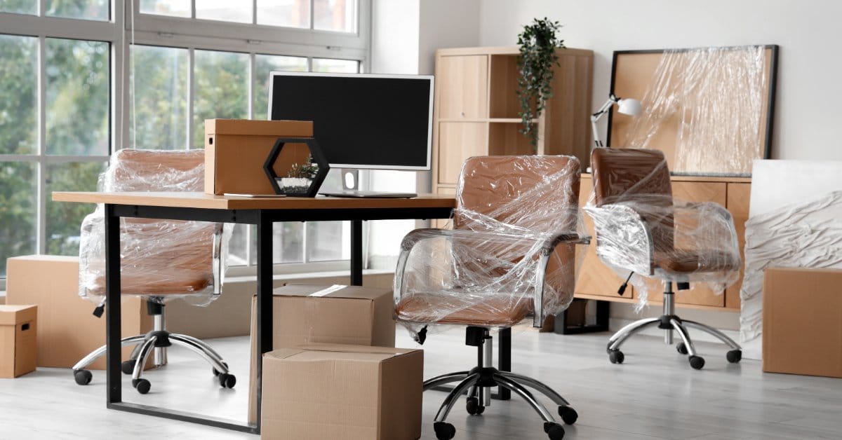 Wrapped used office chairs and a desk waiting for installation in a bright office