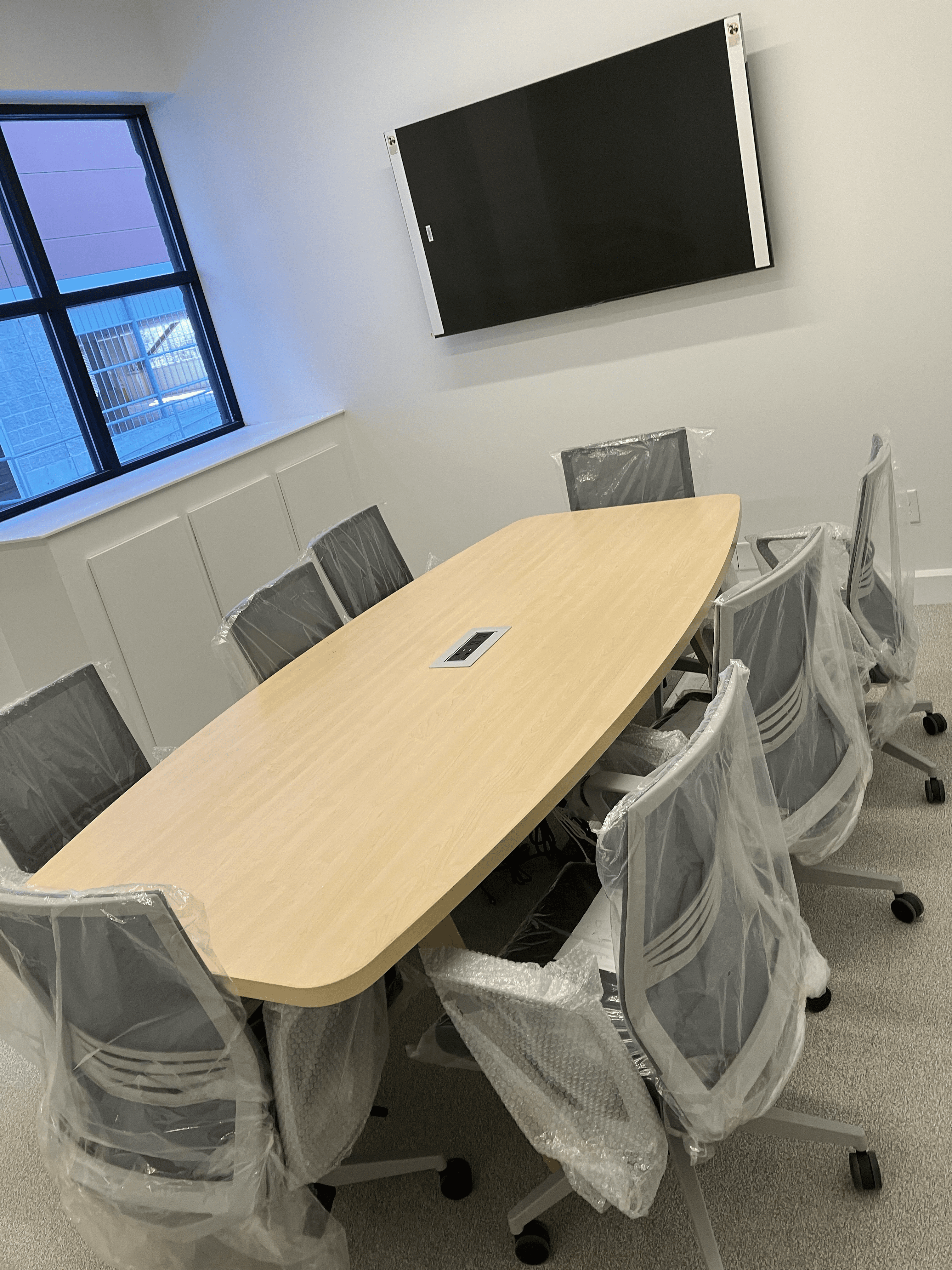 Maple conference table with HDMI, USB, and Power. Eight light grey, contemporary chairs.