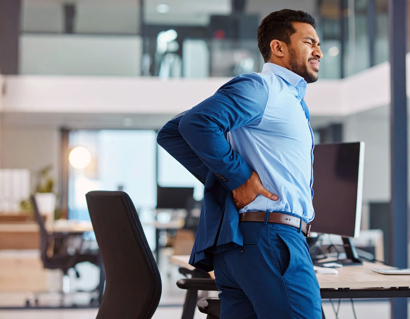 A man dealing with lower back pain due to an uncomfortable office chair.