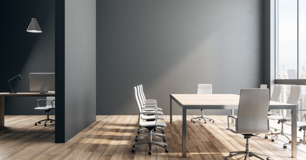 A modern conference room with white office chairs, large meeting table, wood flooring, and floor-to-ceiling windows.